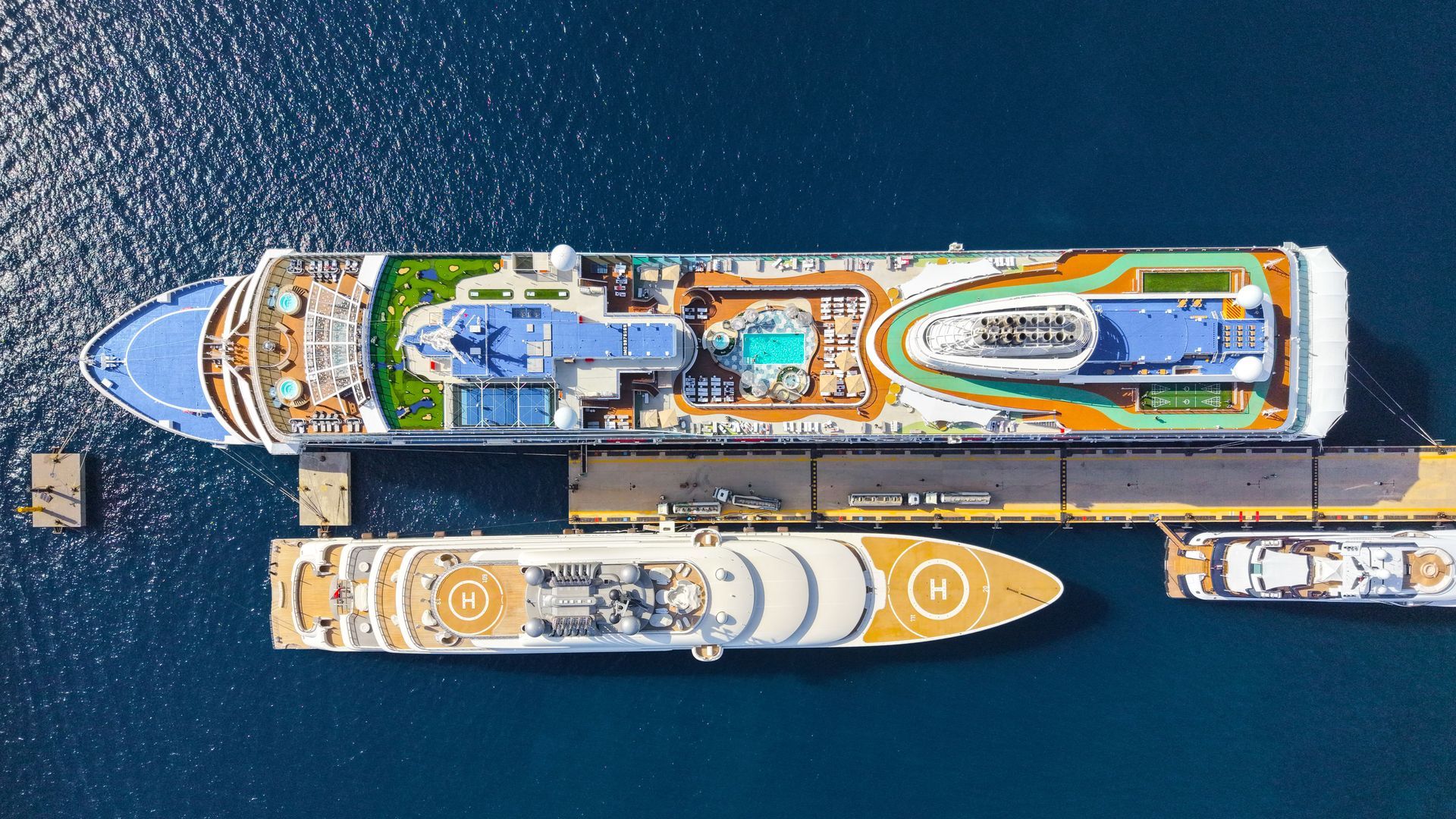 Top-down view of two large cruise ships docked side by side in deep blue water.