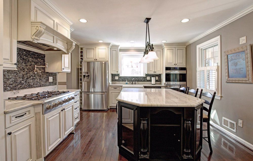A kitchen with white cabinets and stainless steel appliances and a large island in the middle.