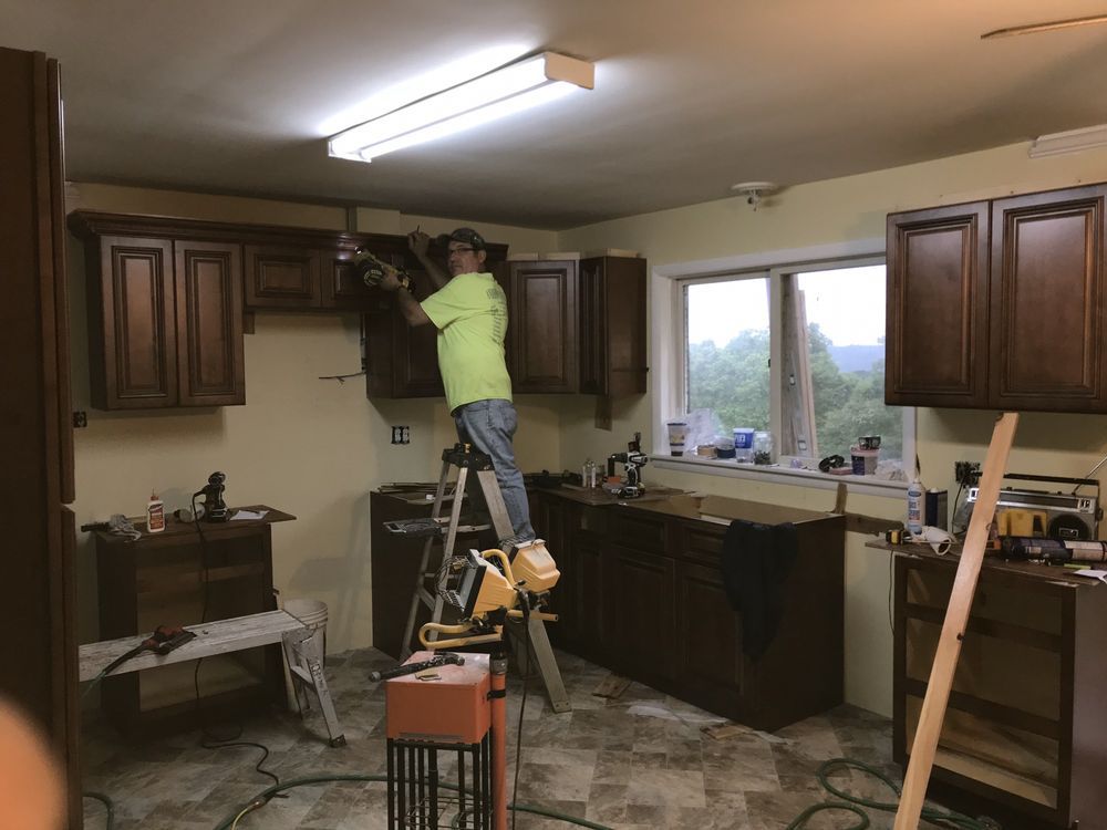 A man is standing on a ladder in a kitchen working on cabinets.