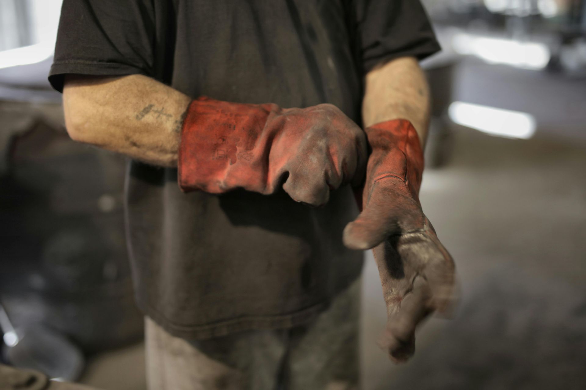 A man is putting on a pair of red welding gloves.