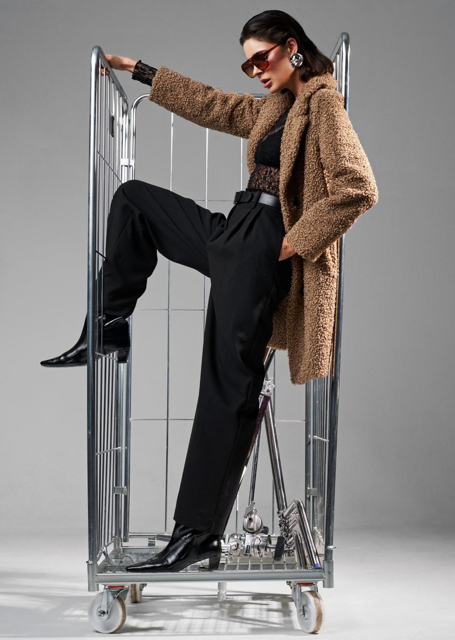 Frau in Leopardenmantel und schwarzer Hose posiert in einem rollenden Metallwagen.