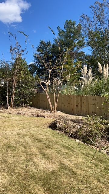 A wooden fence is surrounded by trees and grass in a backyard.