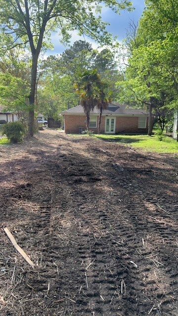 A dirt road leading to a house with trees in the background.