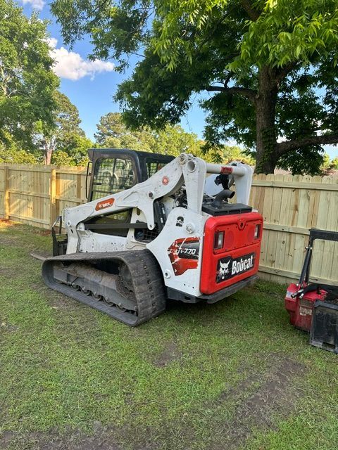 A bobcat skid steer is parked in the grass next to a wooden fence.
