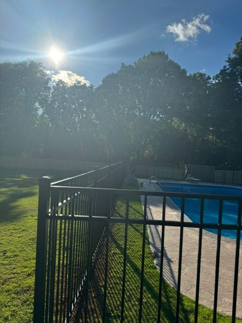 A fence surrounds a swimming pool with the sun shining through the trees