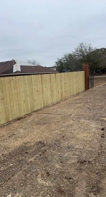 A wooden fence is sitting on the side of a dirt road next to a house.
