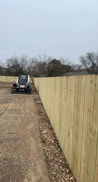A bulldozer is driving down a dirt road next to a wooden fence.