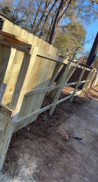 A wooden fence is being built next to a dirt road.