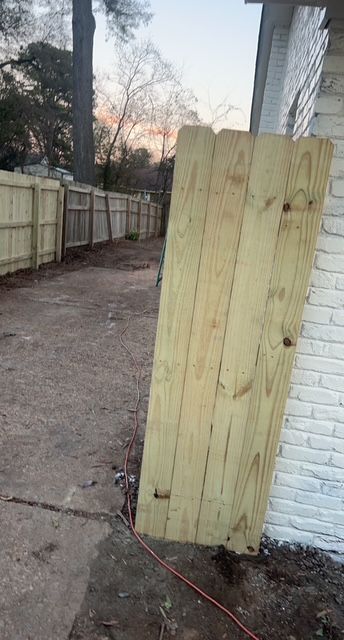 A wooden fence is leaning against a white brick building.