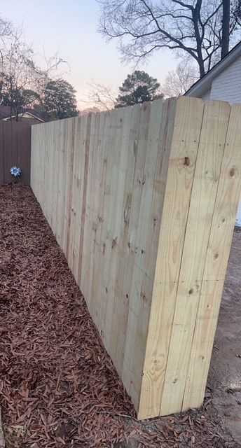 A wooden fence is sitting on top of a pile of mulch next to a house.