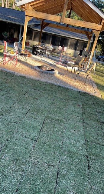 A large lawn with a gazebo and a fire pit in front of a house.