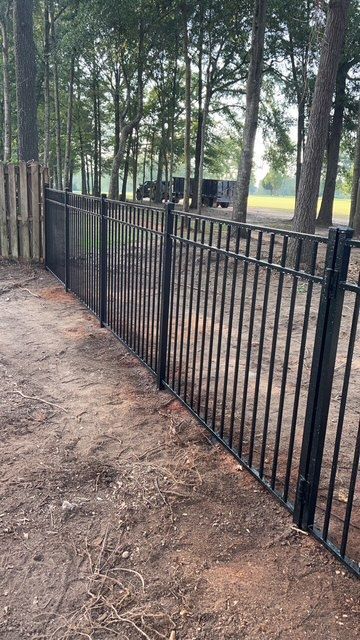 A black metal fence with a wooden fence in the background.