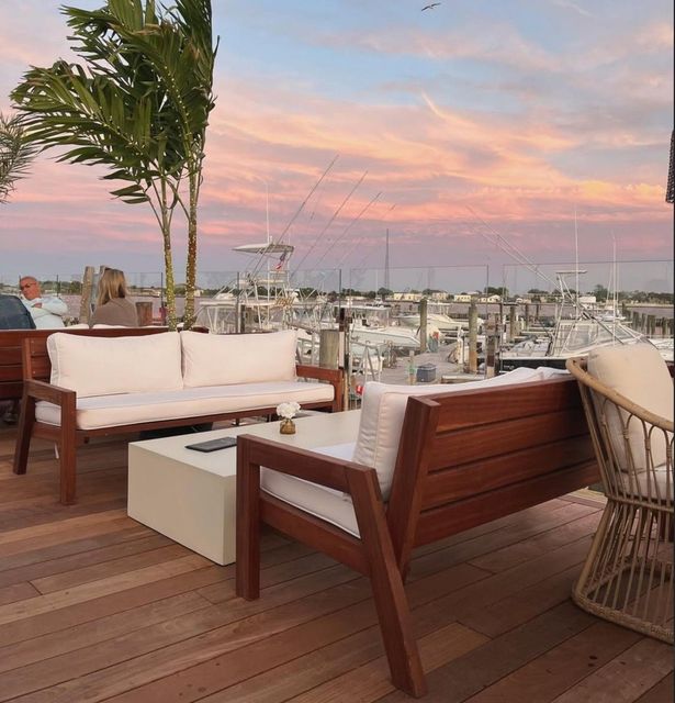 Rooftop lounge with wooden seating and palm tree overlooking a marina at sunset in Cape May, New Jersey