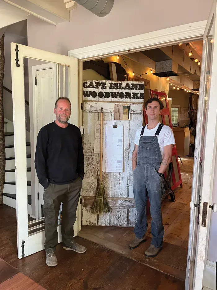 john hassay and brian lee standing in front of a sign that says cape island woodworks