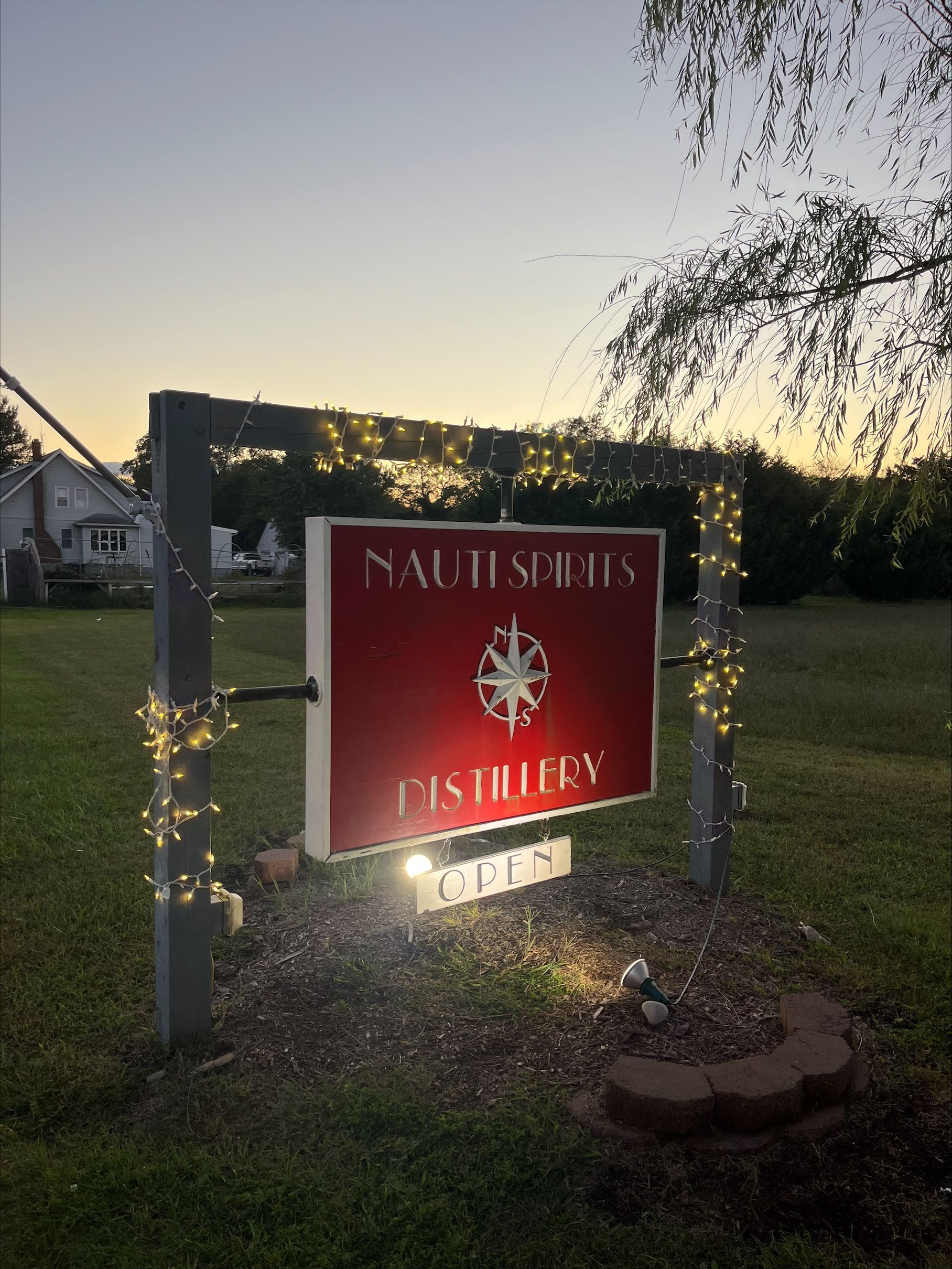 red sign for Nautisaints Distillery with white text and logo, lit up at dusk in cape may new jersey
