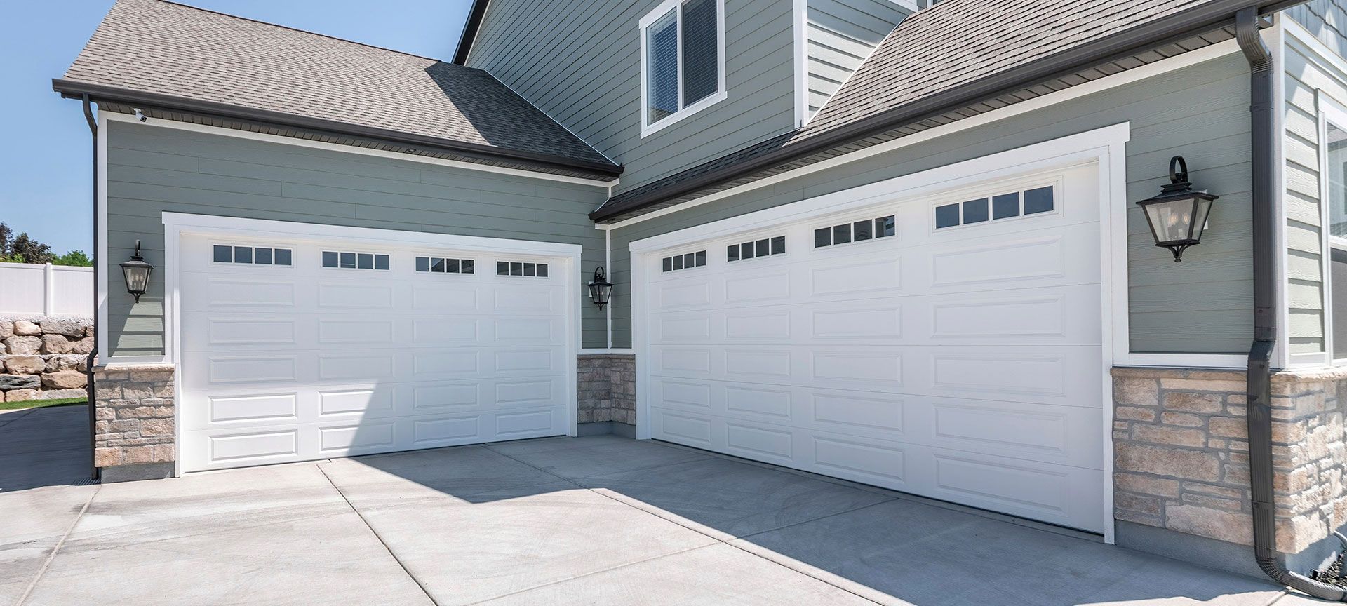 Pano Exterior of a house with concrete driveway and two closed white garage doors with windows 
