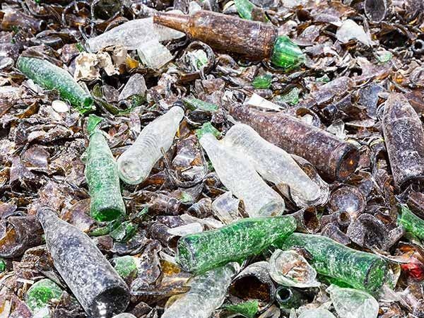 Bottiglie di vetro verdi e trasparenti sparse tra ciottoli e alghe su una spiaggia