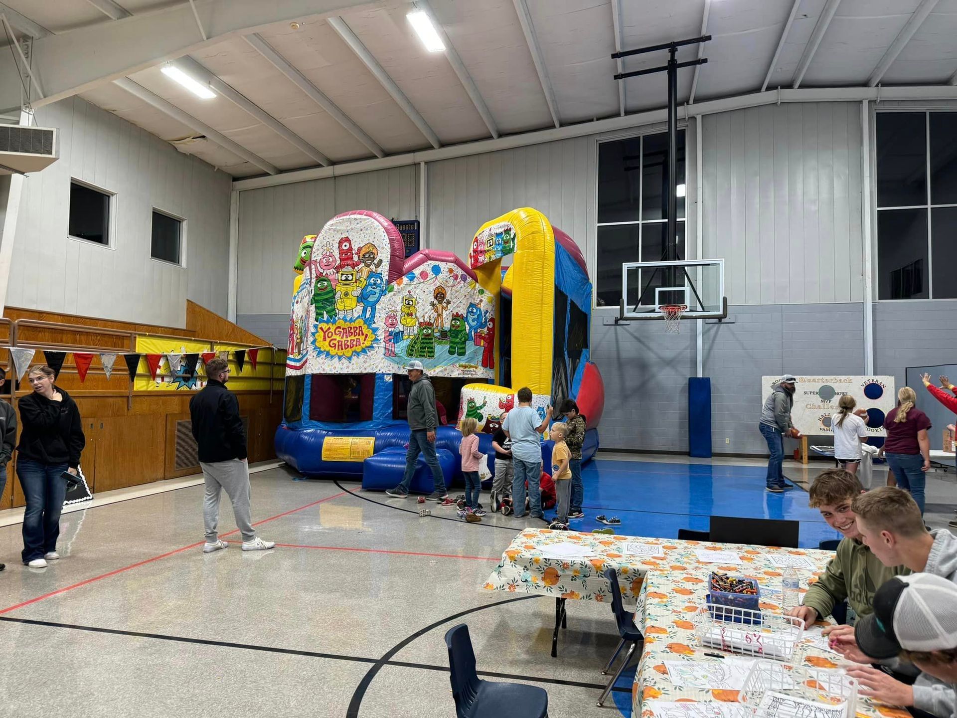 A group of people are standing around a bouncy house in the gym during Octoerfest.
