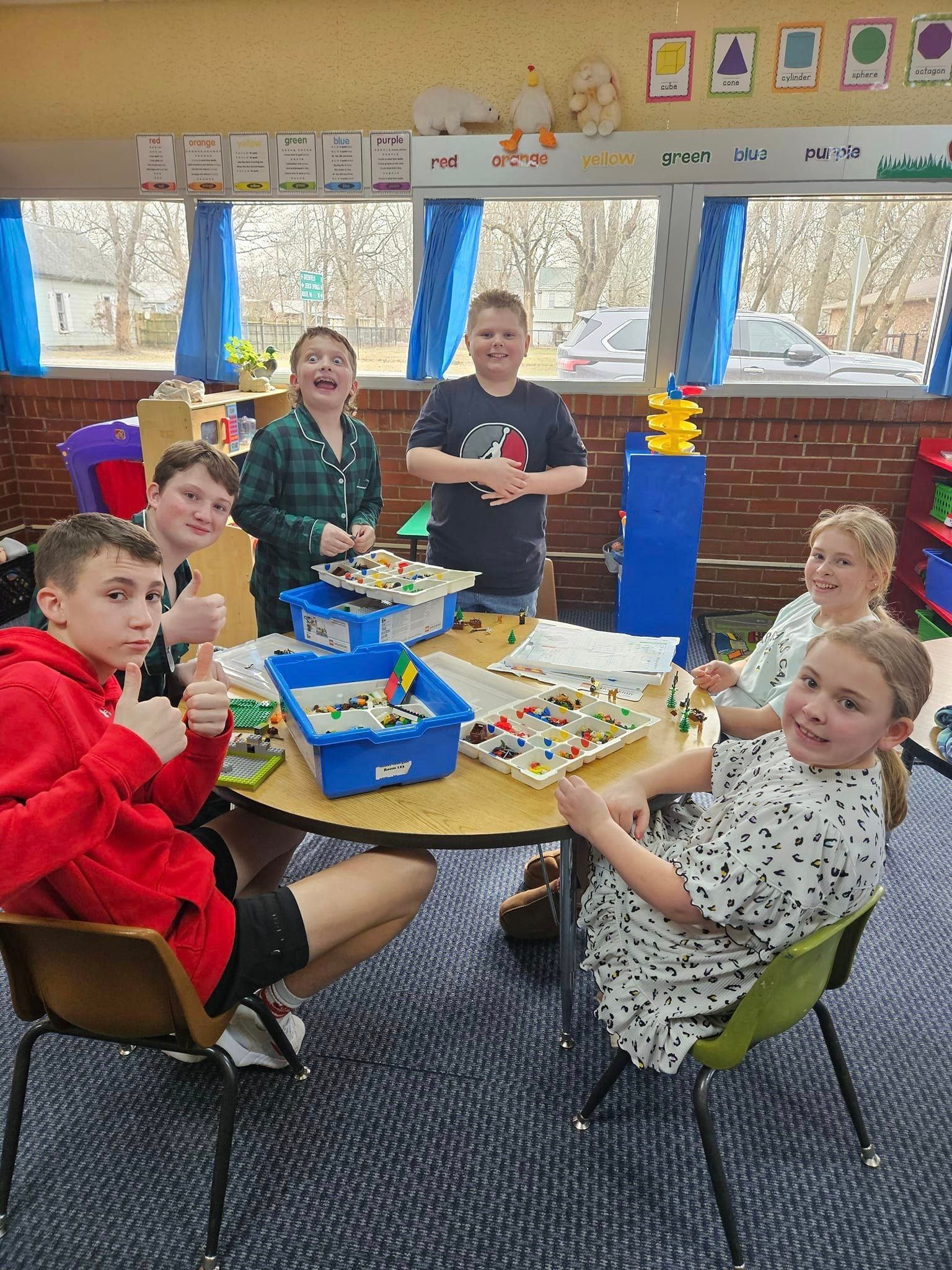 A group of children are sitting around a table in a classroom.