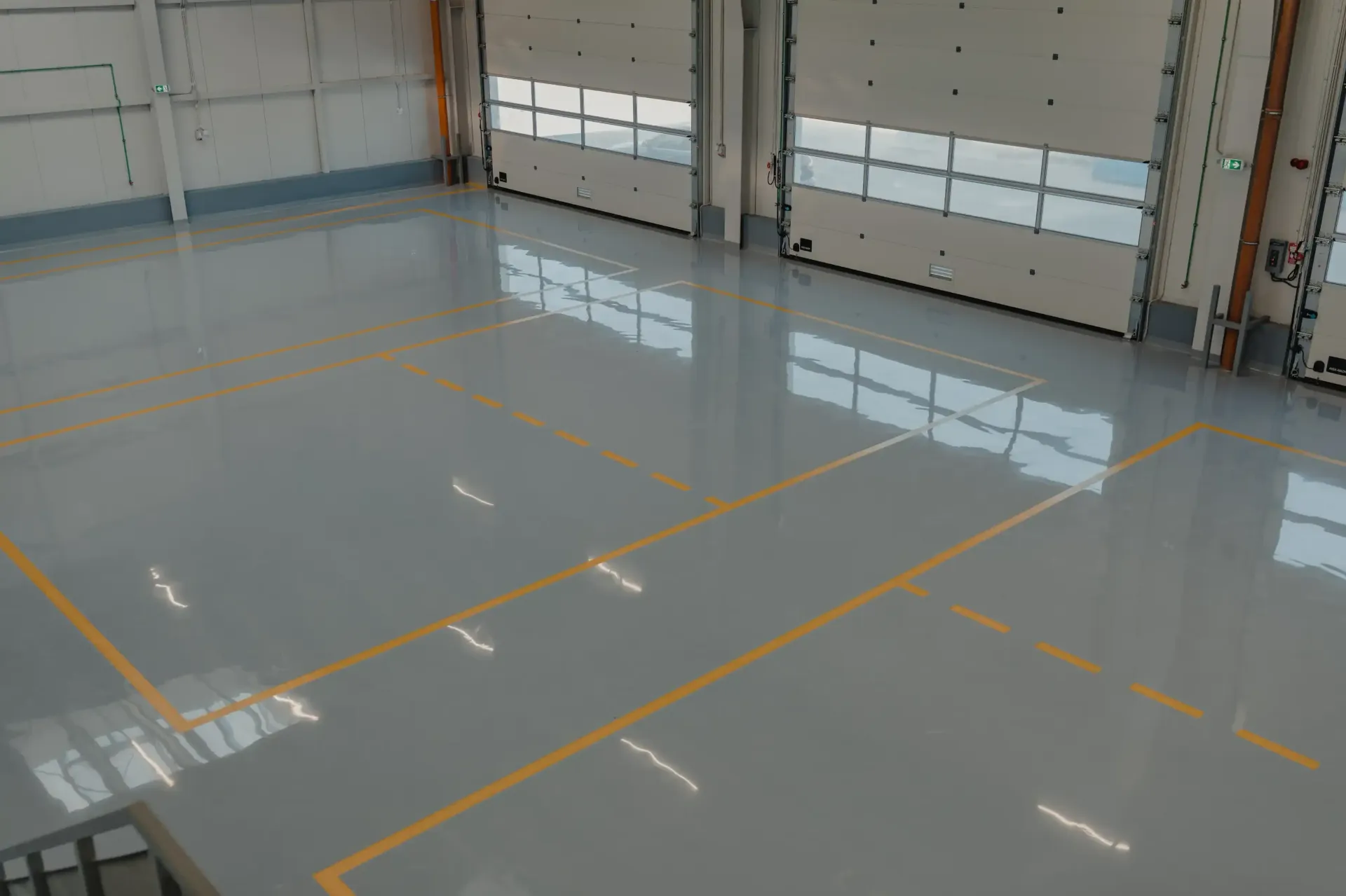 Gray, shiny industrial floor with yellow lines, three garage doors in the background.