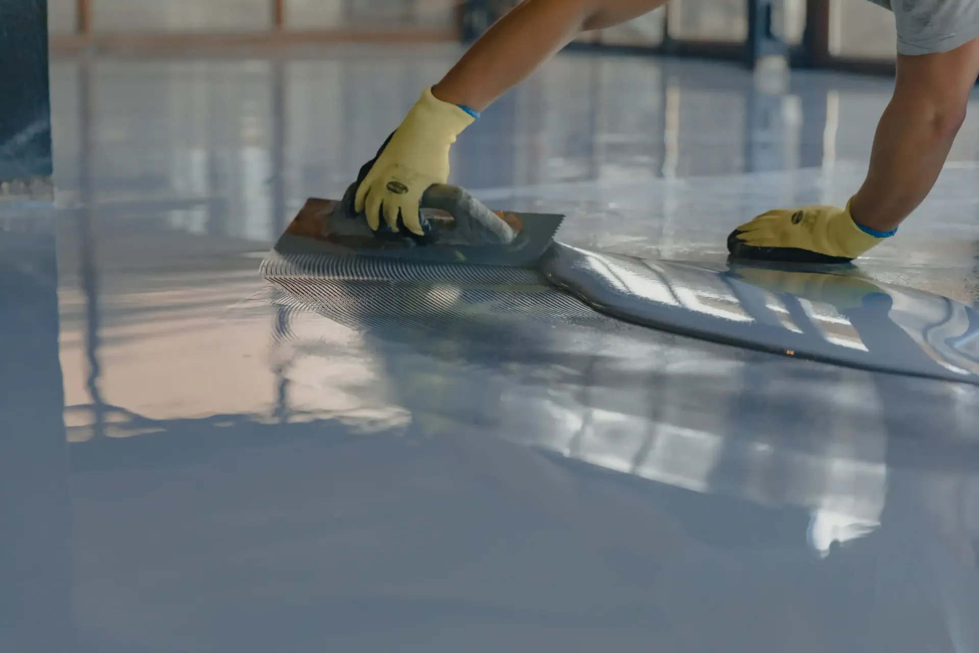 Person in gloves smoothing gray epoxy floor coating with a trowel.