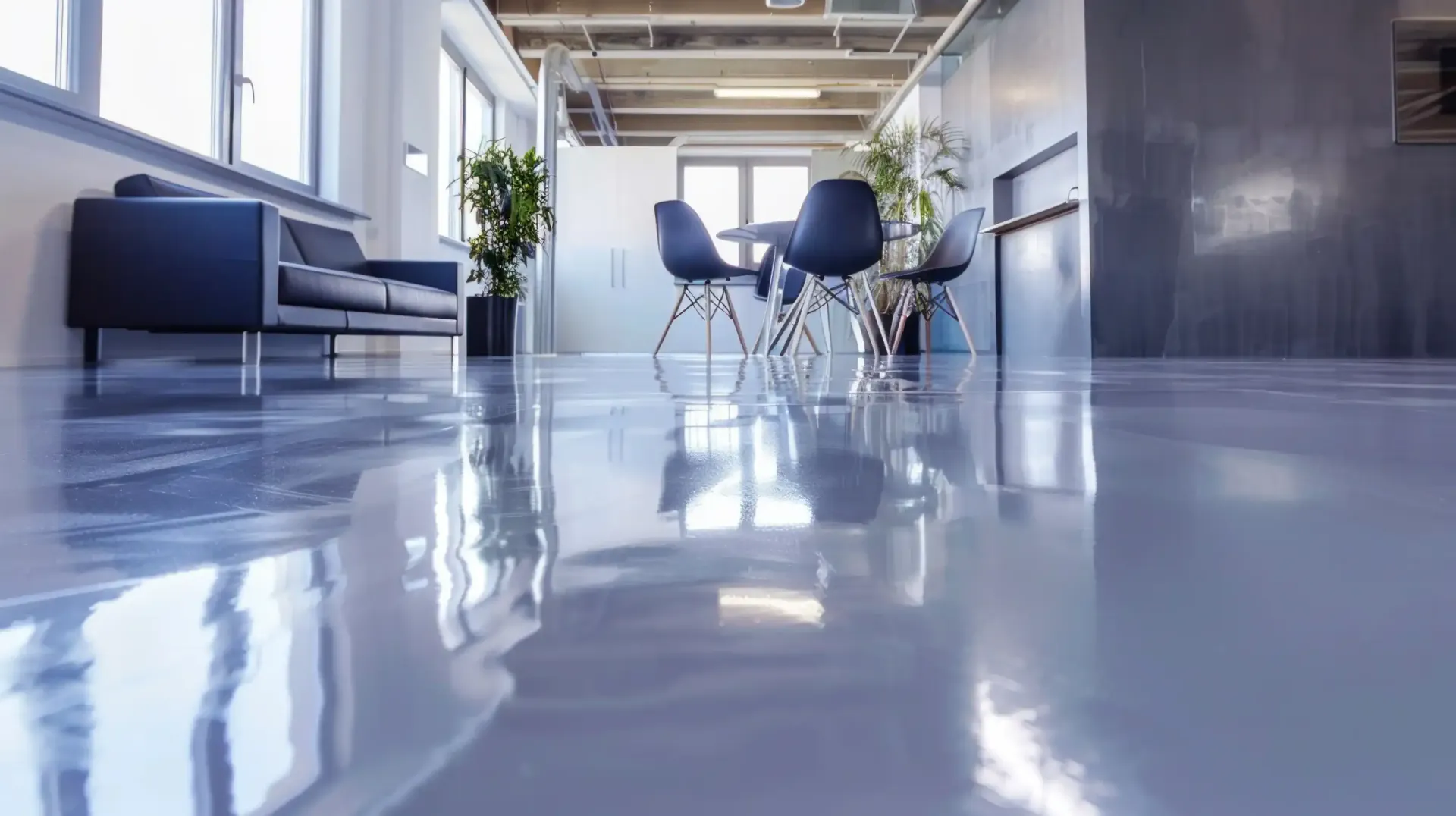 Shiny, gray epoxy floor reflecting a modern office space with furniture and plants.