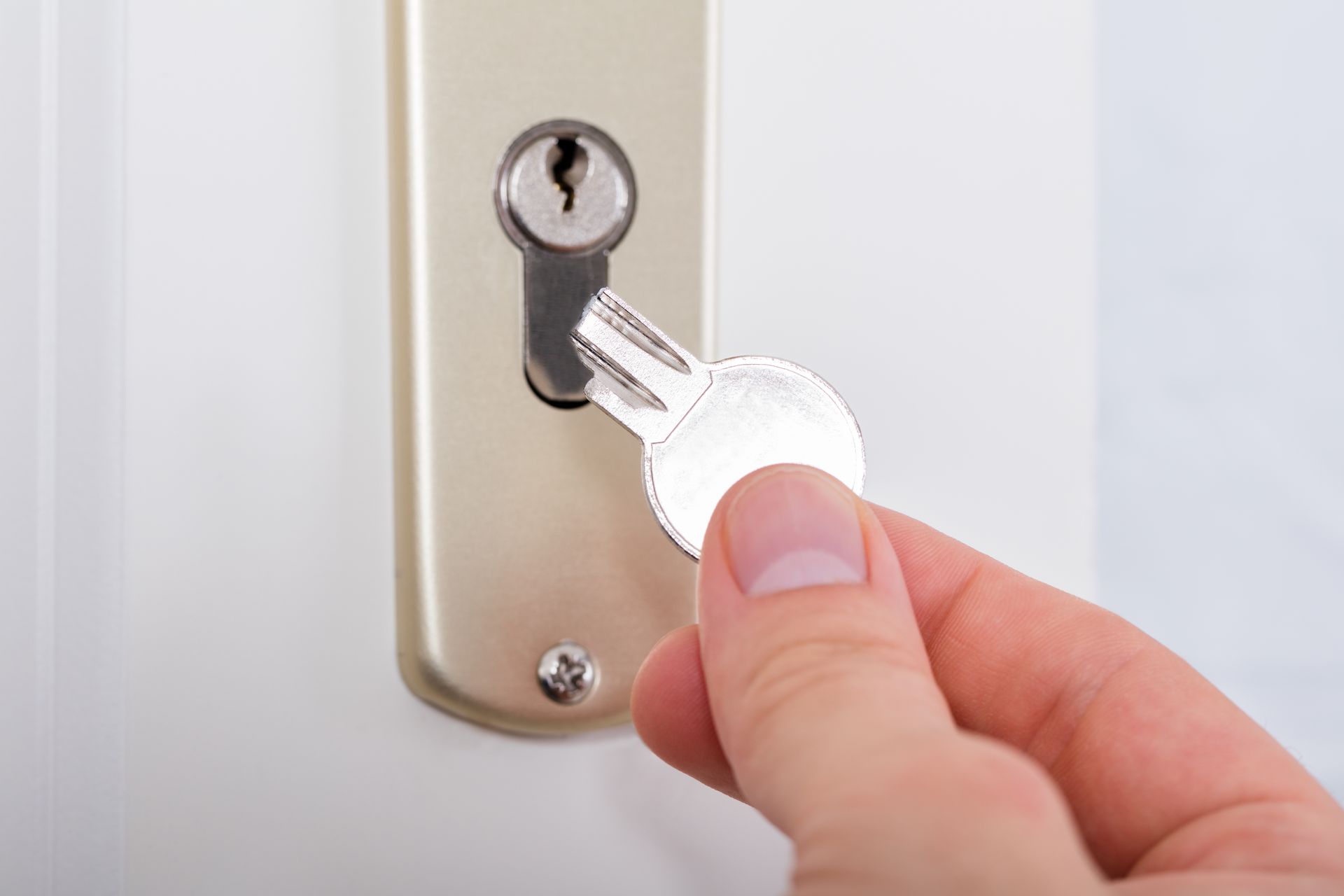 A person is holding a key in front of a door lock.