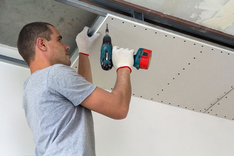 a man in a gray shirt and white gloves working on a ceiling