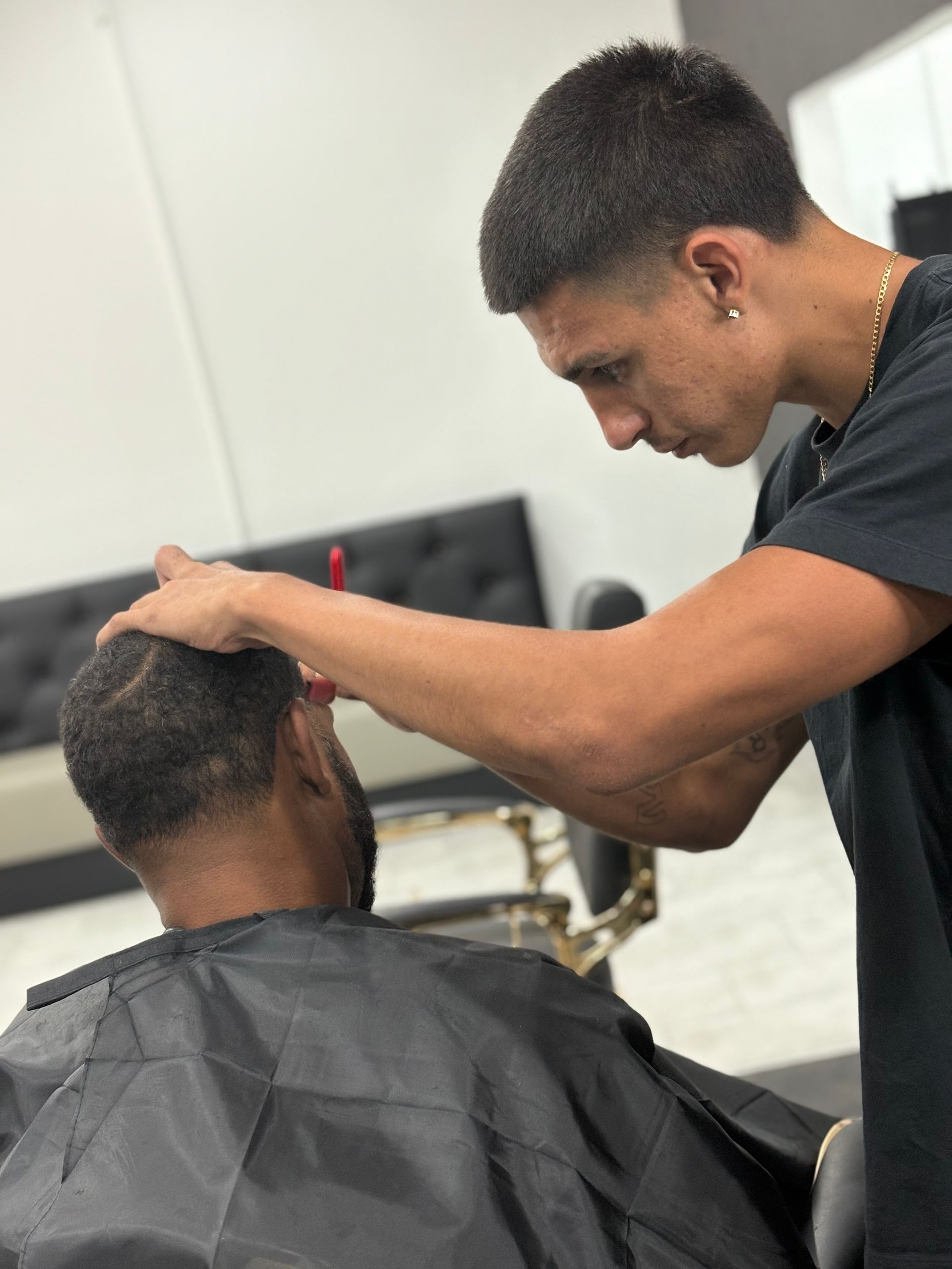 Barber trimming a client's hair in a salon. The barber is wearing a black shirt, and the client is draped in a black cape.