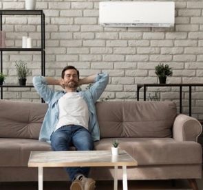 A man is sitting on a couch in a living room with his hands behind his head.