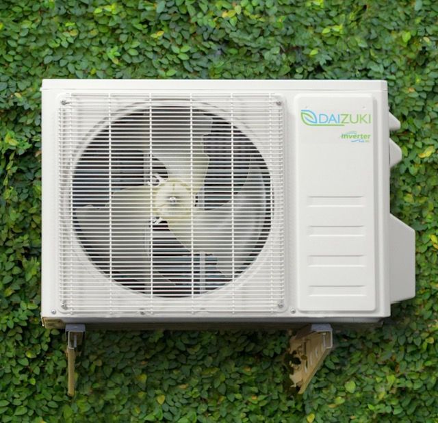 A white air conditioner is mounted to a green wall.