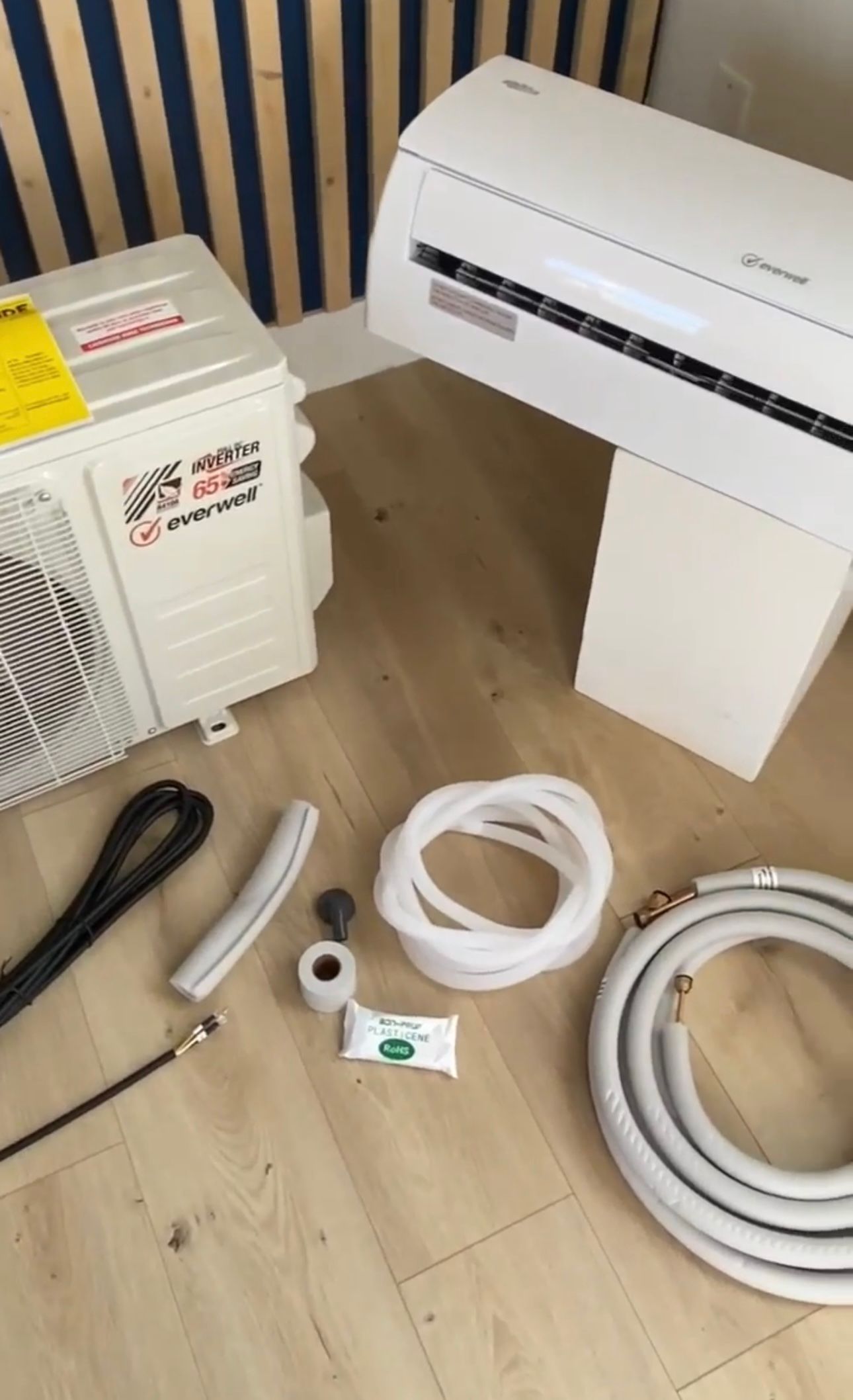 A white air conditioner is sitting on a wooden floor next to a hose.
