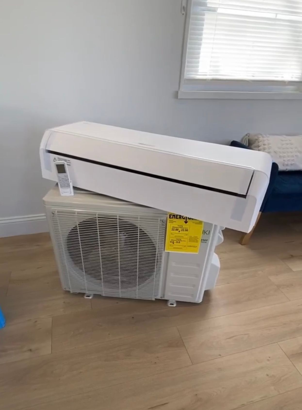 A white air conditioner is sitting on top of a wooden floor in a living room.