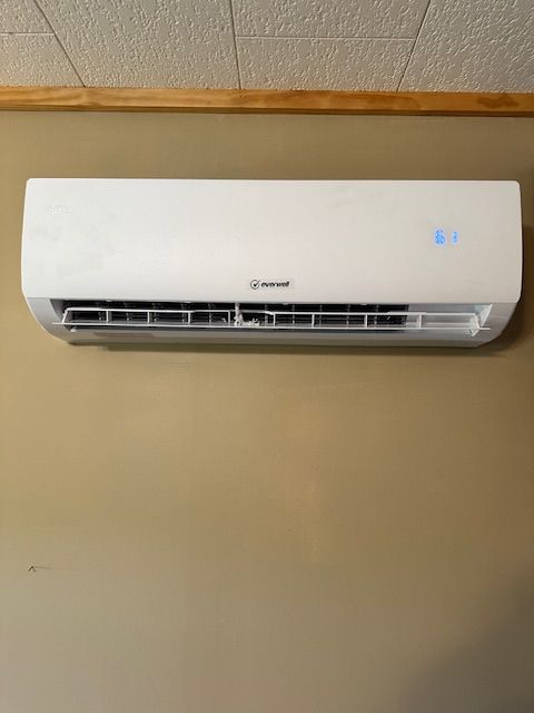 A white air conditioner is hanging on a tan wall.