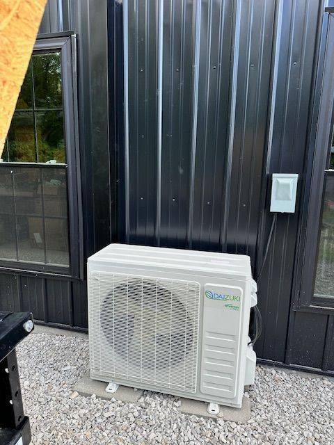 A white air conditioner is sitting in front of a black building.