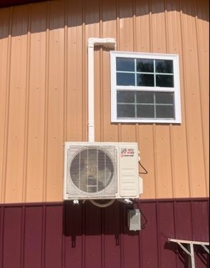 A white air conditioner is mounted on the side of a building next to a window.