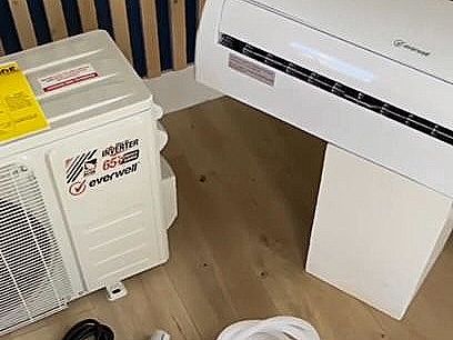 A white air conditioner is sitting on a wooden floor next to a white box.