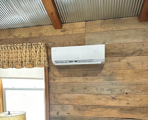 A white air conditioner is hanging on a wooden wall next to a window.