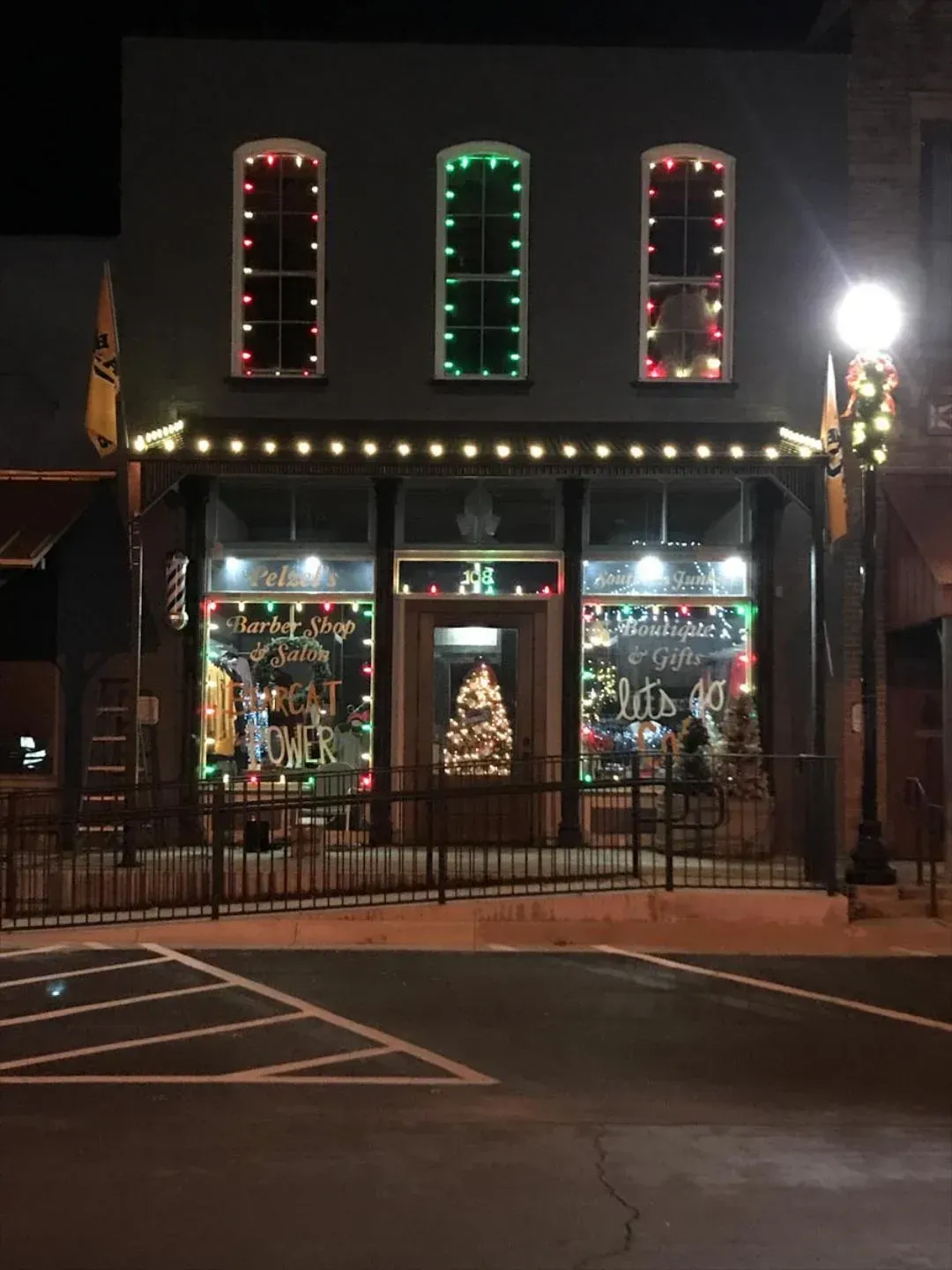 A two-story building decorated for Christmas; string lights on windows and awning. A lit Christmas tree in window.