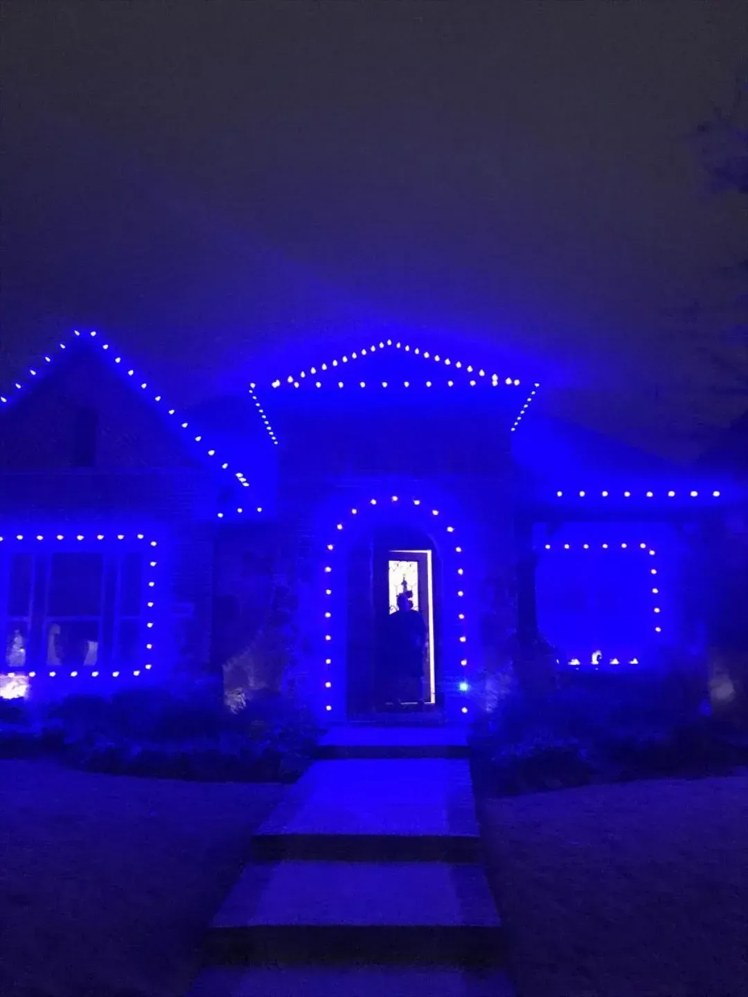 House illuminated with blue lights at night. Entrance with person standing inside.