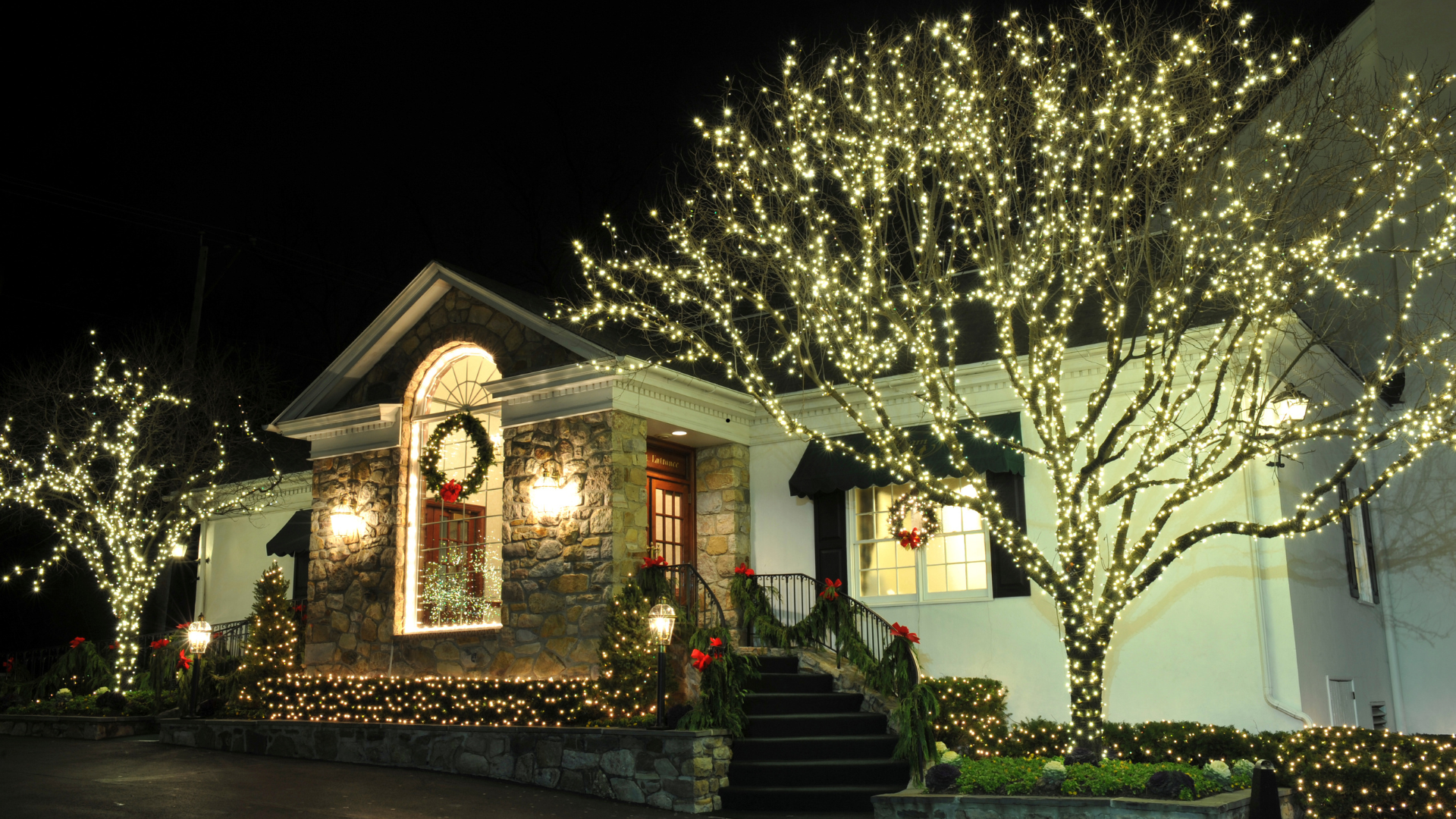 A house decorated with white Christmas lights and wreaths at night.