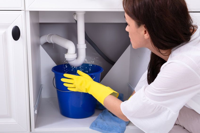 A woman is cleaning a drain under a sink in a kitchen.