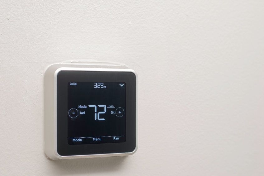 A smart thermostat is hanging on a white wall.
