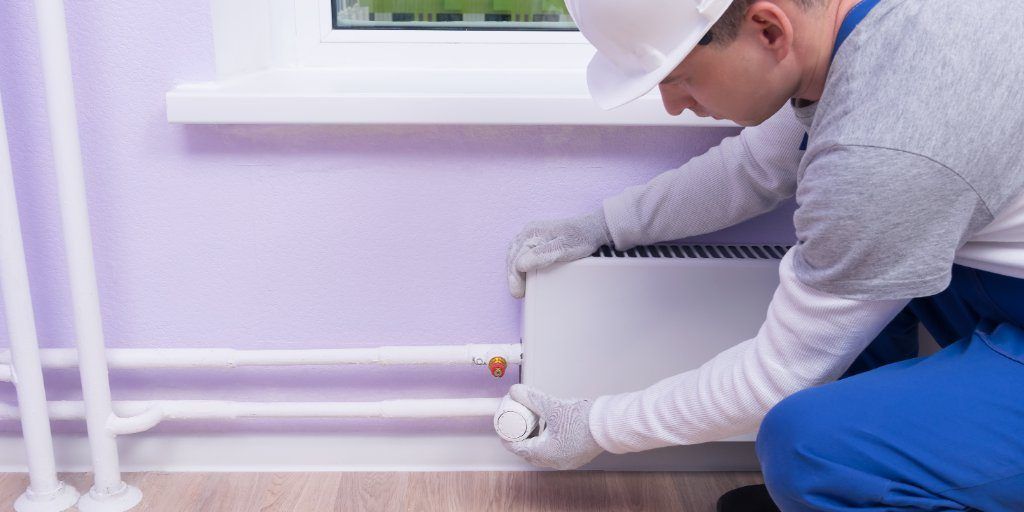 Heating engineer fitting radiator with white plastic pipes - illustrating plastic vs copper piping for home heating systems.