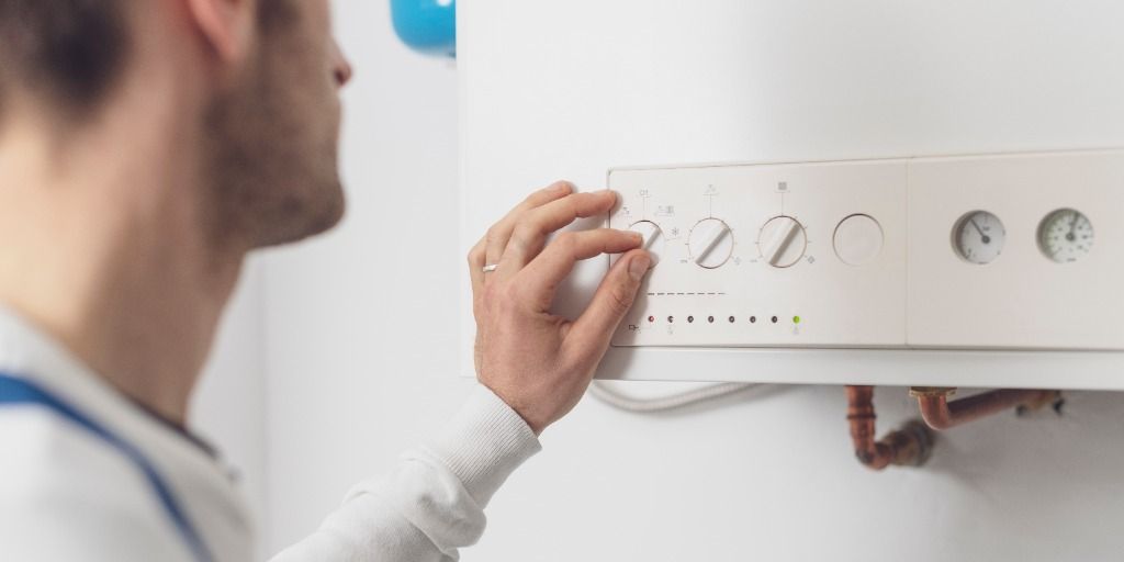 A man is adjusting a boiler on a wall.
