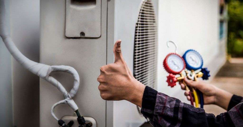 A person is giving a thumbs up while working on an air conditioner.