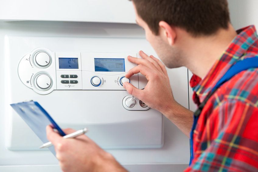 A man is working on a boiler while holding a clipboard and a pen.