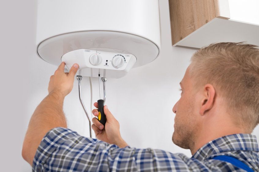 A man is fixing a water heater with a screwdriver.