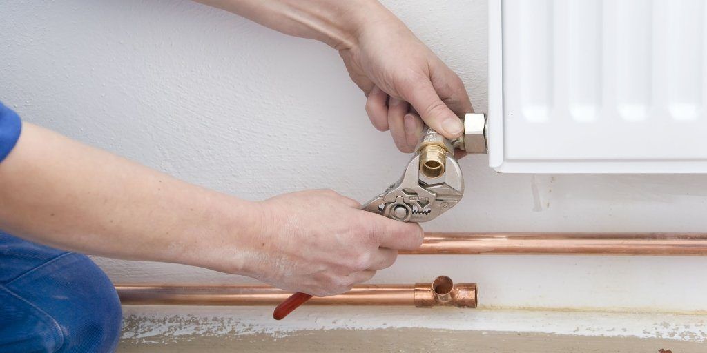 A person is fixing a radiator with a wrench showing Plastic vs Copper Piping