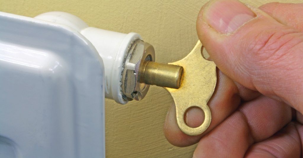 A person is holding a key in front of a radiator.